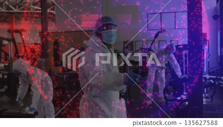 Disinfecting woman in full protective suit spraying treadmill and bench at gym, with sprayer wand 135627588