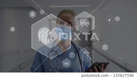 Checking tablet mid adult nurse viewing digital health icons in hospital corridor, with stethoscope 135627596
