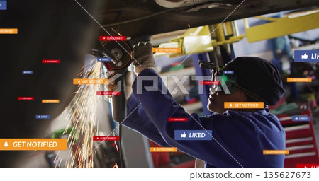 Mechanic wearing gloves grinding under chassis in workshop, with angle grinder sparks, copy space 135627673