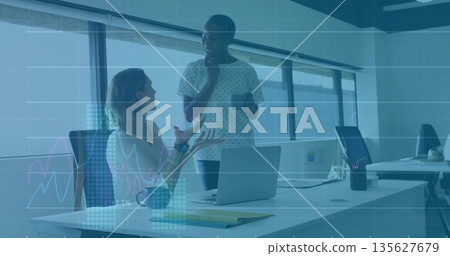 Talking office colleagues gesturing while listening in open-plan office, with laptop coffee mug 135627679