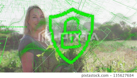 Adult woman holding lettuce in sunlit farmland with crop rows, highlighting digital security theme 135627684