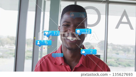 Smiling male influencer standing in modern office by glass windows with floating social media icons Smiling male influencer standing in modern office by glass windows with floating social media icons 135627693