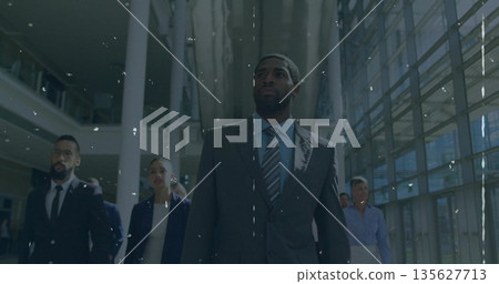 Striding mid adult man leading colleagues in suits through lobby with glass walls and tall columns Striding mid adult man leading colleagues in suits through lobby with glass walls and tall columns 135627713