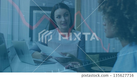 Analyzing financial charts, mid-adult woman holding documents at corporate office with laptop 135627716
