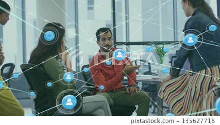 Gesturing diverse colleague wearing red shirt at office desk with monitors and network icons Gesturing diverse colleague wearing red shirt at office desk with monitors and network icons 135627718