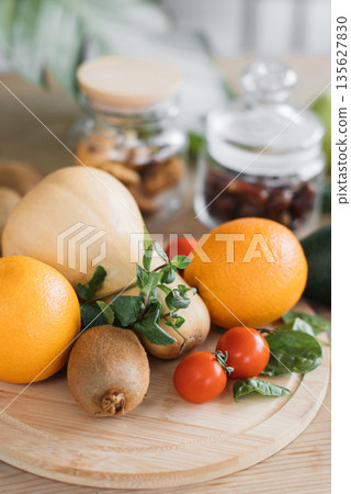 A vibrant collection of fresh produce including oranges, kiwi, butternut squash, tomatoes, and spinach, arranged on a wooden board with jars in the background A vibrant collection of fresh produce including oranges, kiwi, butternut squash, tomatoes, and spinach, arranged on a wooden board with jars in the background 135627830