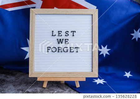 Somber Australian flag backdrop with text LEST WE FORGET on letter board. Respectful message for memorial ANZAC. Concept of remembrance and honor Somber Australian flag backdrop with text LEST WE FORGET on letter board. Respectful message for memorial ANZAC. Concept of remembrance and honor 135628228