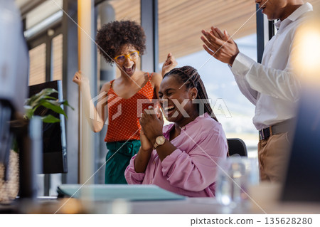 Colleagues celebrating success in office, African American woman smiling joyfully 135628280