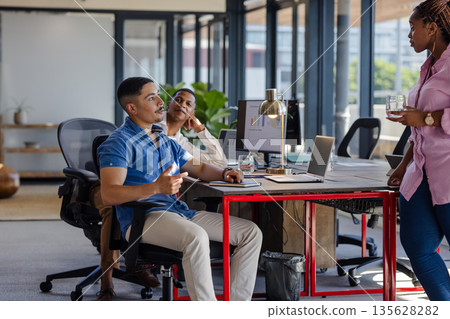 Colleagues discussing project ideas in modern office with laptops and documents 135628282