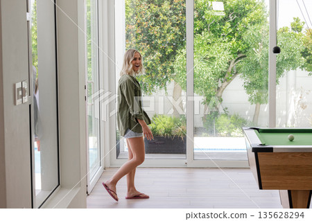Smiling woman in casual outfit walking near pool table in bright living room 135628294