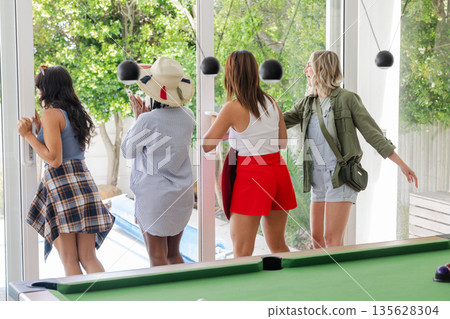 Women enjoying sunny day by pool, laughing and chatting near glass doors 135628304