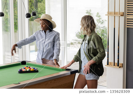African American woman and friend playing pool, discussing strategy at home African American woman and friend playing pool, discussing strategy at home 135628309