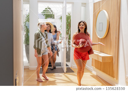 Entering bright home, friends smiling and carrying hats on summer day 135628330