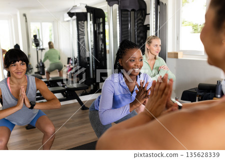 Women exercising in gym, practicing squats with instructor, smiling and focused 135628339