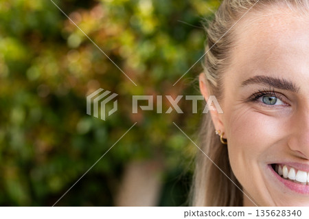Smiling woman outdoors with greenery in background, showing happiness and positivity 135628340