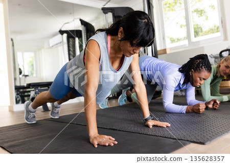 Women exercising in gym, focused on plank position during workout session Women exercising in gym, focused on plank position during workout session 135628357