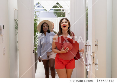 Women entering vacation home, smiling and holding hats, excited for getaway Women entering vacation home, smiling and holding hats, excited for getaway 135628358