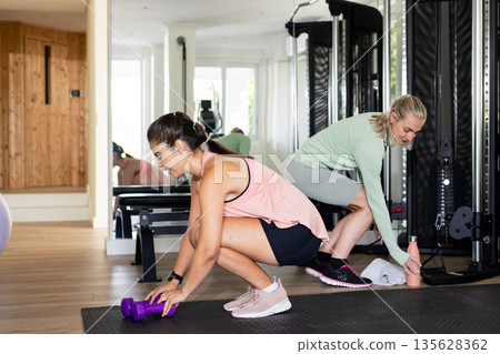 Women exercising in gym, lifting weights and preparing for workout session Women exercising in gym, lifting weights and preparing for workout session 135628362