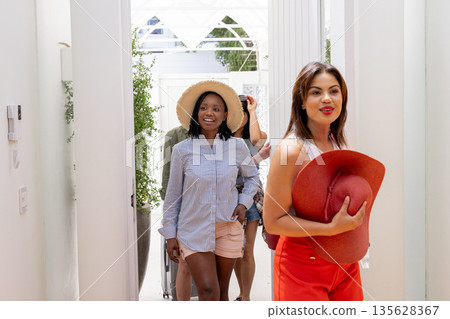 Women entering vacation home, smiling and holding sun hats, enjoying summer getaway 135628367
