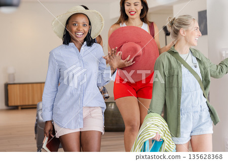 Women enjoying vacation indoors, carrying hats and bags, smiling and chatting 135628368