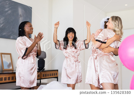 Women in matching robes celebrating at home, smiling and enjoying moment 135628380