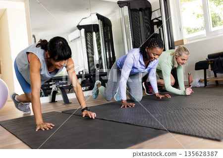 Women exercising on yoga mats in gym, focused on fitness and strength training Women exercising on yoga mats in gym, focused on fitness and strength training 135628387