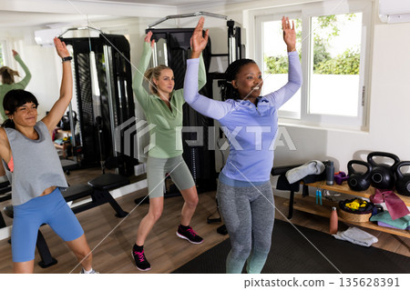 Women exercising together in home gym, lifting arms and staying active Women exercising together in home gym, lifting arms and staying active 135628391