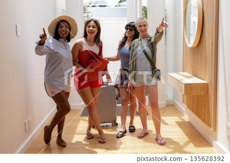 Group of diverse women excitedly preparing for vacation with suitcase in hallway Group of diverse women excitedly preparing for vacation with suitcase in hallway 135628392