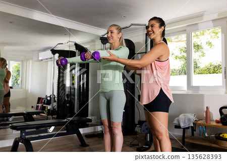 Women exercising with dumbbells in home gym, smiling and enjoying workout together Women exercising with dumbbells in home gym, smiling and enjoying workout together 135628393
