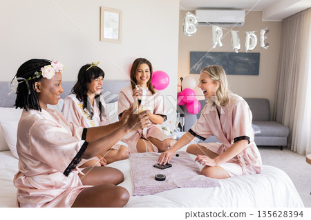 Laughing and playing games, diverse women in robes celebrating bachelorette party Laughing and playing games, diverse women in robes celebrating bachelorette party 135628394