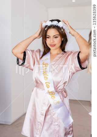 Bride-to-be adjusting veil, wearing satin robe, preparing for wedding celebration 135628399