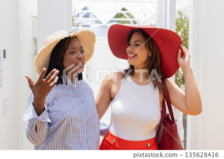 Two women wearing sun hats enjoying conversation at home, smiling and relaxed Two women wearing sun hats enjoying conversation at home, smiling and relaxed 135628416