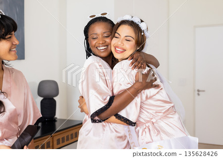 Women in silk robes hugging and smiling, celebrating friendship at home 135628426