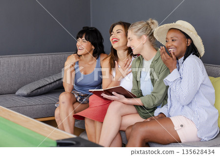 Diverse group of women laughing together on couch, enjoying leisure time indoors Diverse group of women laughing together on couch, enjoying leisure time indoors 135628434