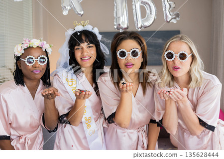 Women in matching robes blowing kisses at bachelorette party, wearing fun sunglasses 135628444