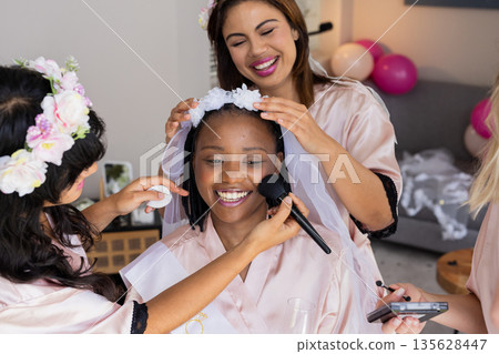 Women preparing bride with makeup and flowers, smiling and enjoying celebration 135628447