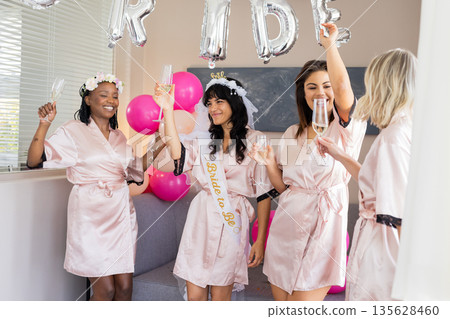 Women in satin robes celebrating with champagne at bridal shower party 135628460