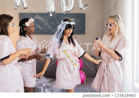 Opening champagne, women in robes celebrating bachelorette party with excitement Opening champagne, women in robes celebrating bachelorette party with excitement 135628483