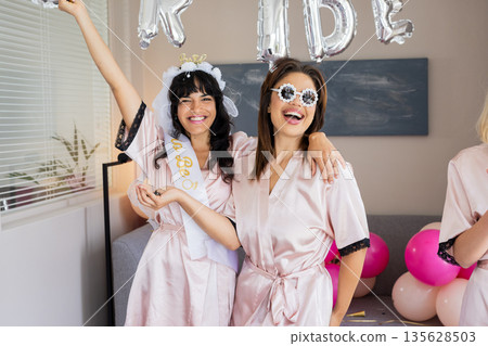 Celebrating bachelorette party, women in robes smiling with balloons and decorations 135628503