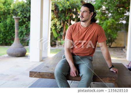 Man sitting on outdoor table, looking away, enjoying peaceful garden view Man sitting on outdoor table, looking away, enjoying peaceful garden view 135628510