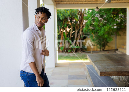 Young man standing on patio, looking away thoughtfully, enjoying outdoor space Young man standing on patio, looking away thoughtfully, enjoying outdoor space 135628521