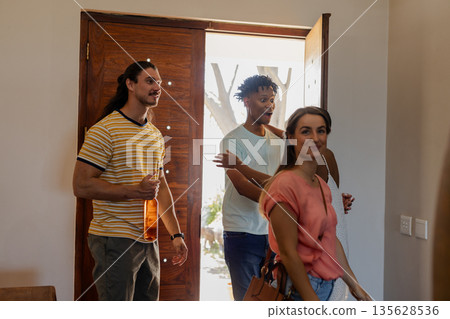 Friends arriving at home, smiling and holding drinks, enjoying casual gathering 135628536