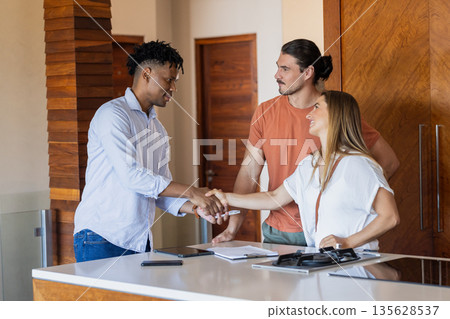 Real estate agent shaking hands with couple in modern kitchen, finalizing agreement 135628537