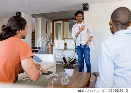 At home, man standing and gesturing while friends listen during conversation At home, man standing and gesturing while friends listen during conversation 135628540