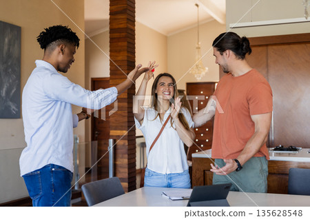 Friends celebrating success together at home, smiling and high-fiving around tablet Friends celebrating success together at home, smiling and high-fiving around tablet 135628548