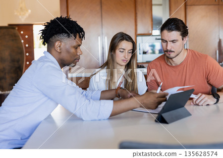 Diverse friends collaborating on project with tablet and documents at home Diverse friends collaborating on project with tablet and documents at home 135628574