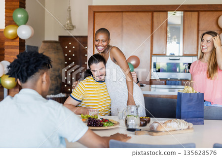 Friends celebrating at home, enjoying food and laughter around dining table 135628576