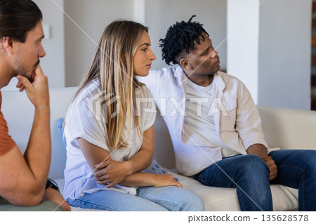 Friends sitting on sofa having thoughtful conversation in cozy living room Friends sitting on sofa having thoughtful conversation in cozy living room 135628578