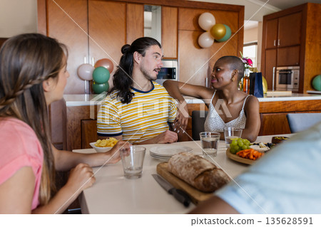Friends enjoying conversation and snacks at home around dining table 135628591
