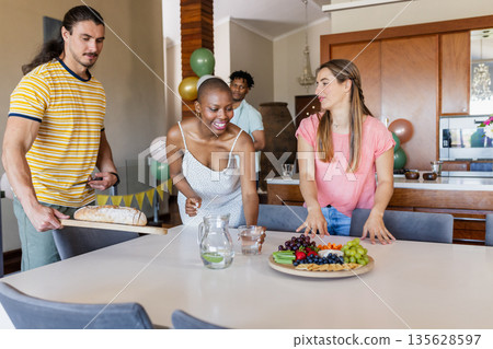 Friends preparing table with fresh bread, fruits, and drinks for casual gathering Friends preparing table with fresh bread, fruits, and drinks for casual gathering 135628597